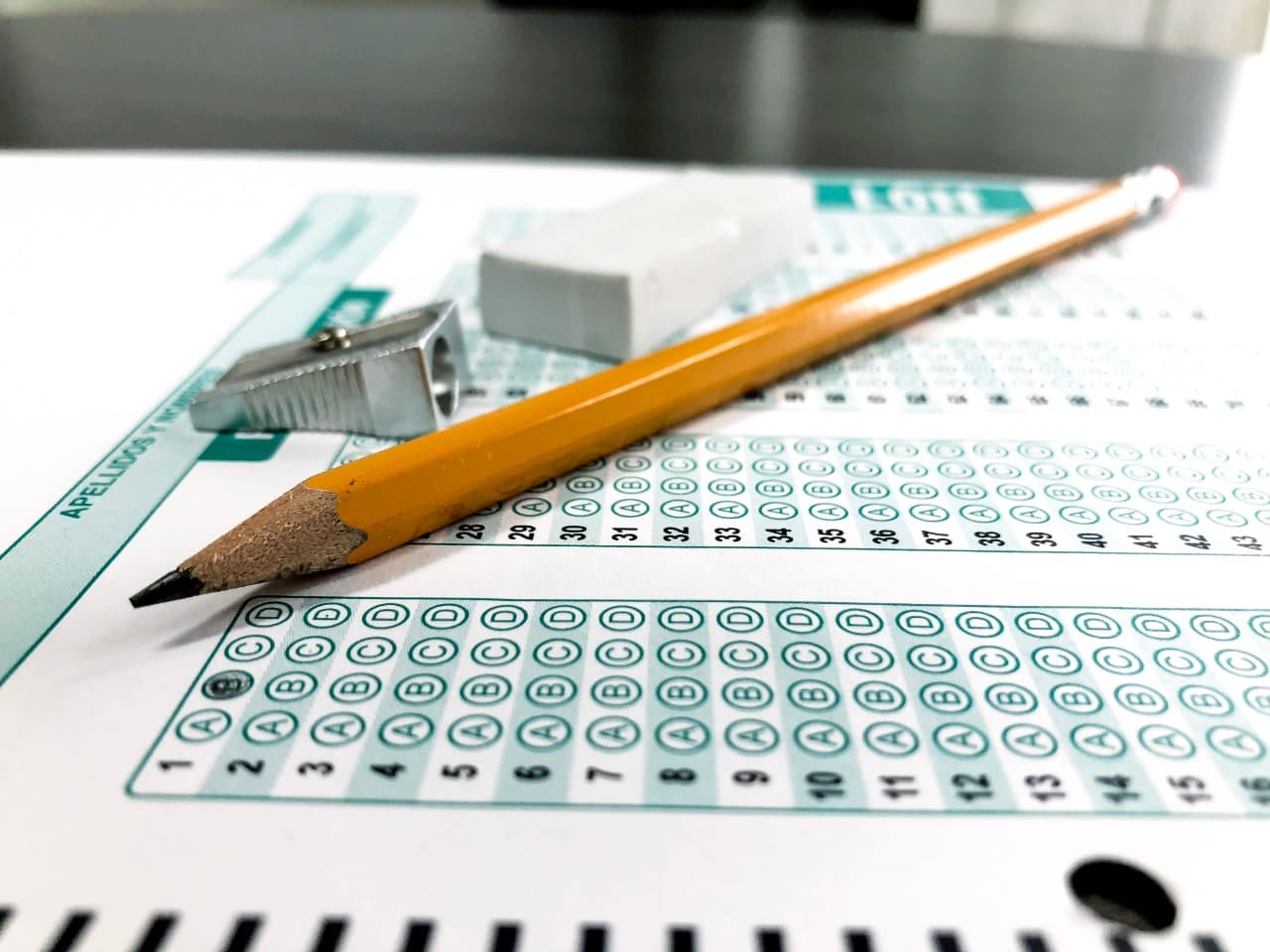Imagen de hoja de respuesta de examen con un lápiz, un tajalápiz y un borrador encima.